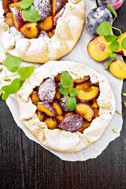 Parşömen üzerinde erik, şeker ve kakule ile iki tatlı turta, yukarıdan ahşap bir arka planda yeşil nane filizi