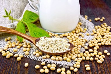 Kaşık içinde soya unu, cam sütte süt, soya fasulyesi ve arka planda çuval bezi üzerinde yaprak.