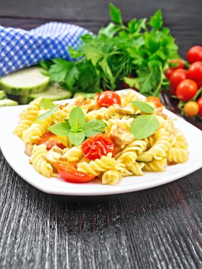 Tavuklu Fusilli, kabaklı ve domatesli bir tabak, peçete, çatal, fesleğen ve maydanoz.