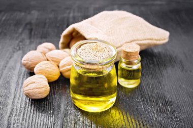 Kavanozda ceviz yağı ve bir şişe, bütün fındıklar çantada ve masada, siyah tahta tahtaya karşı.