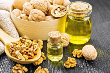 Cam şişede ceviz yağı ve kavanoz, fındıklar kutuda, kaşıkta ve masada, çuval bezi siyah tahta arka planda.