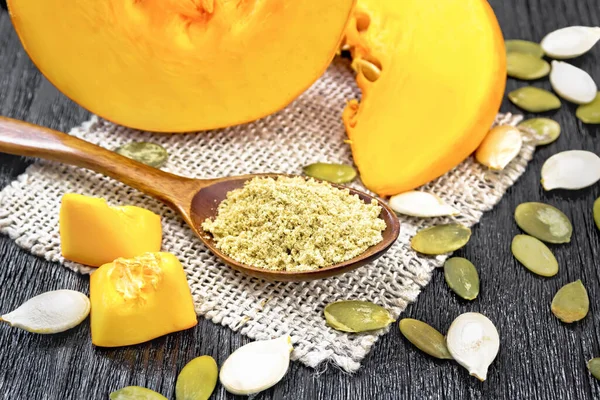 Çuval bezinde bir kaşıkta kabak unu, tahtanın arka planında bir sebzenin tohumları ve dilimleri.