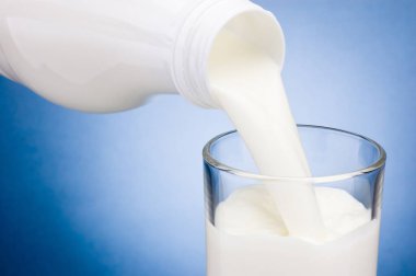Mavi arka plan üzerinde cam içine plastik şişe süt dökme