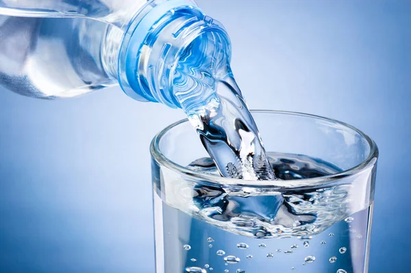 Verter agua de la botella en vidrio sobre fondo azul — Foto de Stock