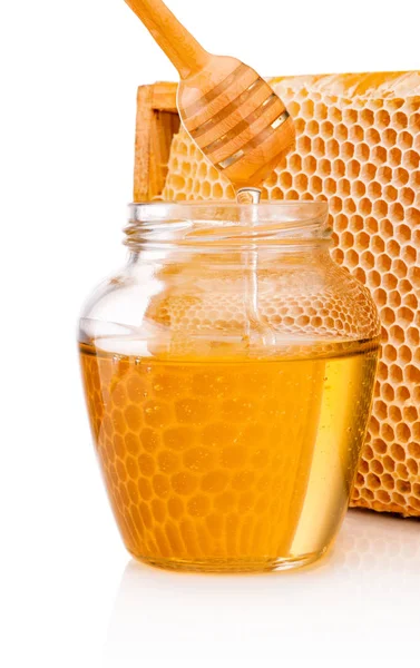 Honey dripping from dipper into glass jar on background honeycom — Stock Photo, Image