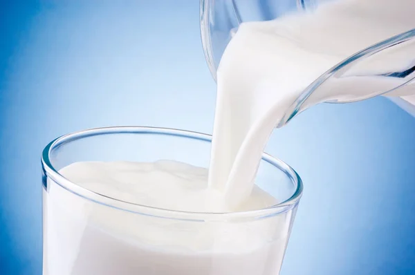 Pouring fresh milk into glass from jug on blue background — Stock Photo, Image