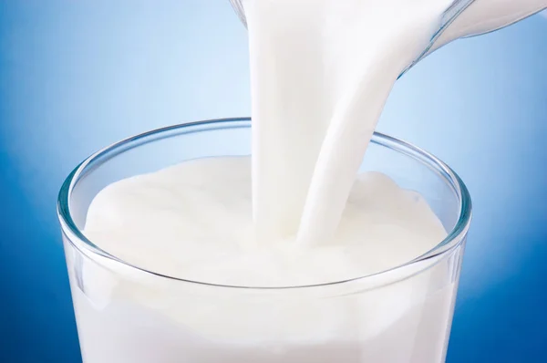 Выливание свежего молока в стакан на голубом фоне — стоковое фото