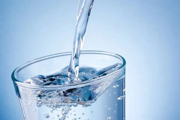 Water in glas gieten op blauwe ondergrond — Stockfoto