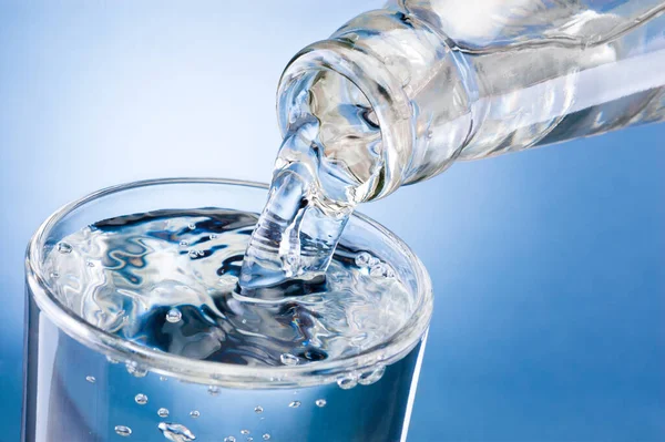 水从瓶子里倒入一个与白色背景隔离的杯子里 — 图库照片