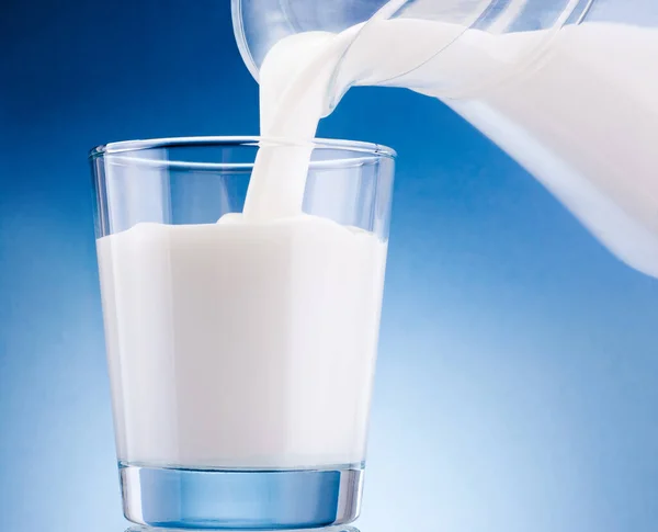 Melk Gegoten Uit Kruik Glas Een Blauwe Achtergrond — Stockfoto