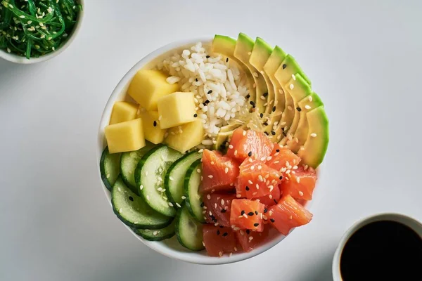 Ham organik Poke ile kase pirinç, avokado, somon, mango, salatalık, chuka salata ve beyaz masa artalanını soya sosu yakın çekim. Üstten görünüm