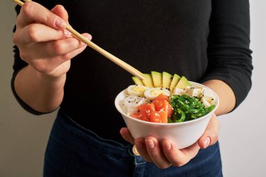yemek çubukları kase somon, avokado pilav ile poke tutan eller, Chuka salata, peynir, bıldırcın yumurtası ile arka plan beyaz ve siyah susam serpilir.