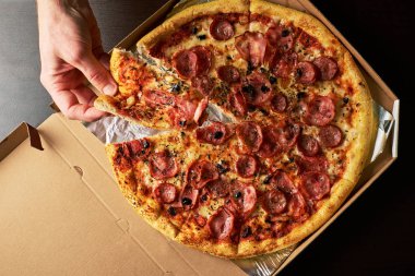 Elini çift peynirli pizza karanlık tablo arka plan ile tüm pizza tepsisinden dilim tutuyor.
