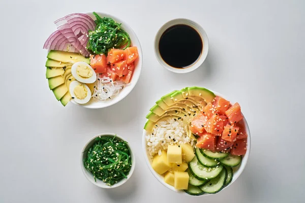 Ham organik Poke bir kase ile pirinç, avakado, somon, mango, salatalık, chuka salata, Bıldırcın yumurta, tatlı soğan ve beyaz masa artalanını soya sosu iki tabak yakın çekim.