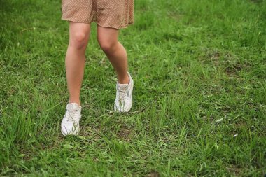 Kız çimlerde yürüyor. Kadın beyaz spor ayakkabı ve elbise yeşil çimenlerin üzerinde çalışır