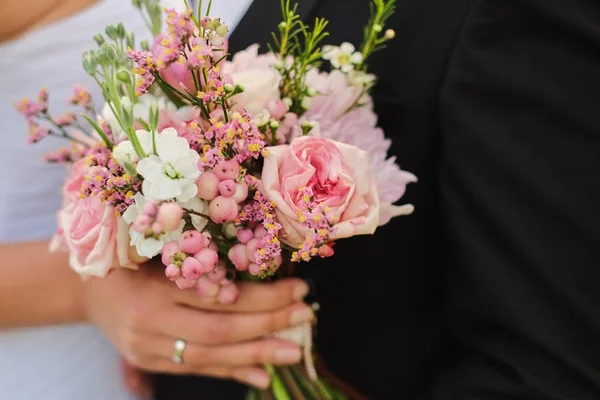 bride holds a wedding bouquet in hands, the groom hugs her