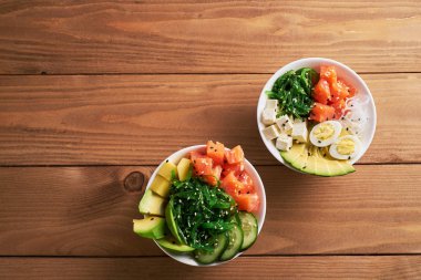 Ham organik Poke bir kase ile pirinç, avakado, somon, mango, salatalık, chuka salata, Bıldırcın yumurta tatlı soğan ve soya sosu iki tabak yakın çekim ahşap arka plan üstten görünüm