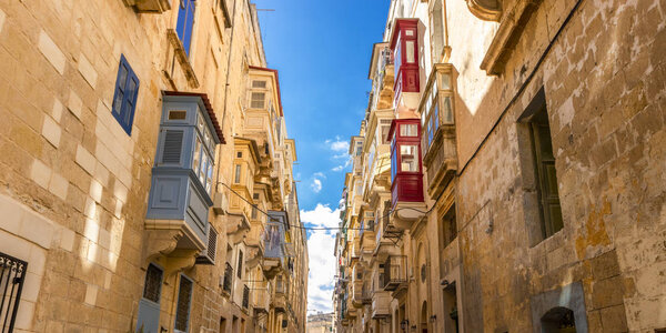 Typical narrow maltese streets with colorful traditional windows and wooden shutters and balconies, clear blue sky on a summer day, Valletta, Malta