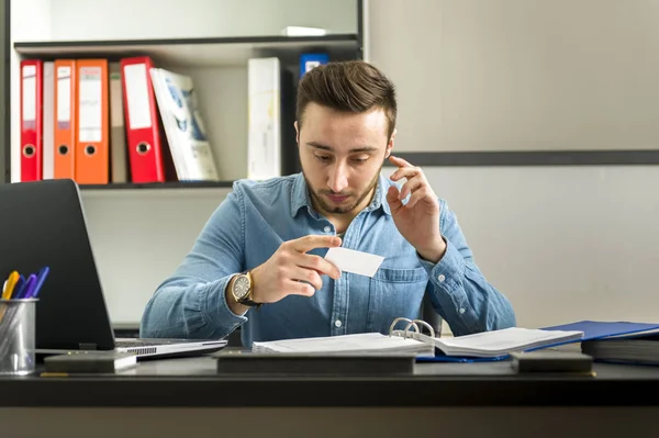 Un jeune homme au bureau regarde la carte de visite — Photo