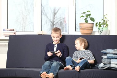 İki kardeş sarışın erkek mavi bir kanepe evde annesiyle akıllı telefonlar çalmaya