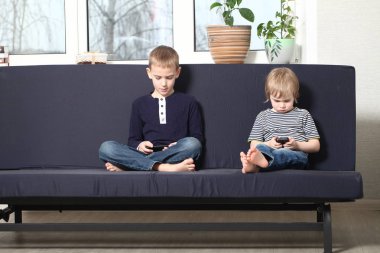 İki kardeş sarışın erkek mavi bir kanepe evde annesiyle akıllı telefonlar çalmaya