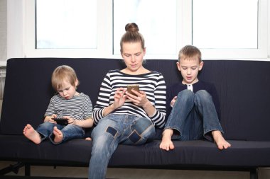 İki kardeş sarışın erkek mavi bir kanepe evde annesiyle akıllı telefonlar çalmaya