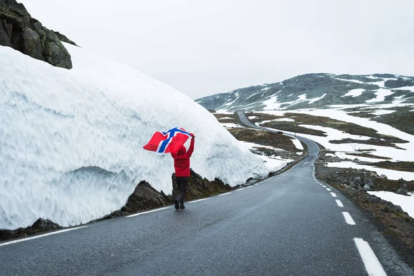 Bjorgavegen ノルウェーの雪道 雪の壁の近くの山道にノルウェーの旗を持つ少女 深刻な北の風景 — ストック写真