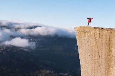 Preikestolen - amazing rock in Norway. Guy on a cliff above the clouds. Pulpit Rock, the most famous tourist attraction in Ryfylke, towers over the Lysefjord clipart