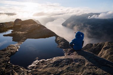 Preikestolen (Müezzin kayası), Ryfylke, ünlü turistik cazibe yakınındaki Lysefjord üzerinde kuleleri. Adam bir kayanın üzerinde mesafe içine bakıp şafak sahiptir