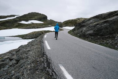 Norveç doğal manzaralı rota Aurlandsfjellet. Dağ yolundan Bjorgavegen Norveç'te mavi bir ceket bir adam yürüyor