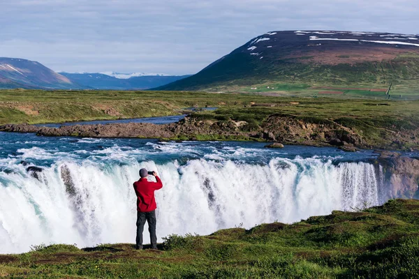 Godafoss şelale. İzlanda'daki güzel manzara. Kırmızı ceketli çocuk bir fotoğraf nehir kenarında yapar.