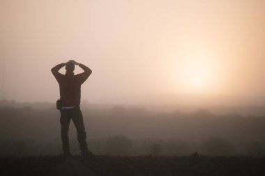 Yükselen güneşe bakarak adam düşünüyor. Sabah yatay, sis, İzlanda