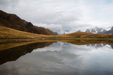 Bulutlar bir ayna yansıması ile dağ gölü. Ana Kafkas ridge görünümünü. Uzun yürüyüşe çıkan kimse tepede duruyor. Koruldi,: Samegrelo zemo svaneti, Georgia