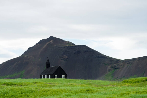 Black Church in the village of Budir, Iceland. Religious and tourist attraction. Summer landscape with a chapel and a mountain top