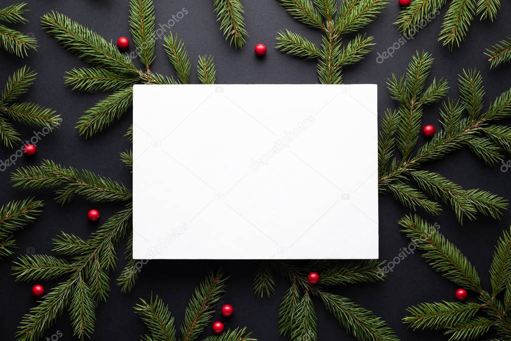 Christmas holiday background with copy space for text. Flat lay, top view. Decorative frame of fir branches and holly berries. Paper notice sheet
