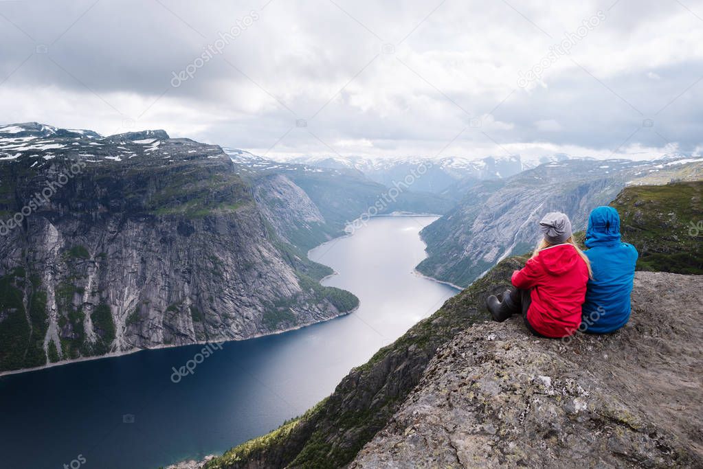 Trolltunga -  most spectacular Norway sights. Couple of travelers sits on rock and looks at Ringedalsvatnet Lake