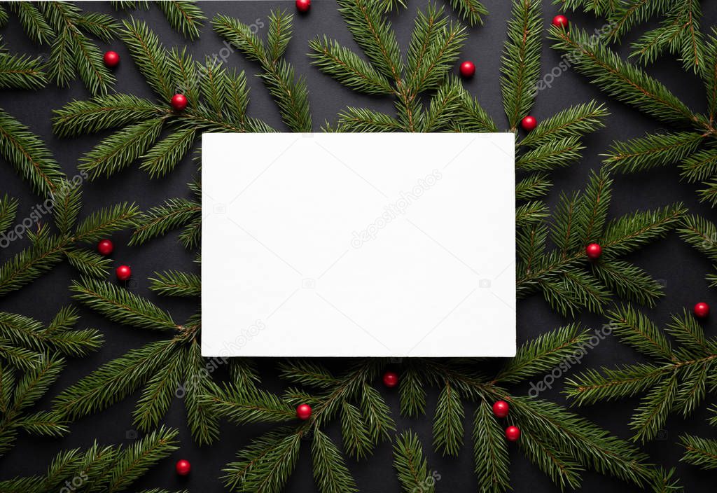 Christmas border. New Year background with copy space for text. Flat lay, top view. Decorative frame of fir branches and holly berries. Paper notice sheet