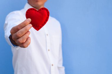 Happy Valentine's Day için tebrik kartı. Adam mavi duvar arka plan üzerinde kırmızı bir kalp aşk sembolü olarak verir. Kopya alanı Festival konseptiyle