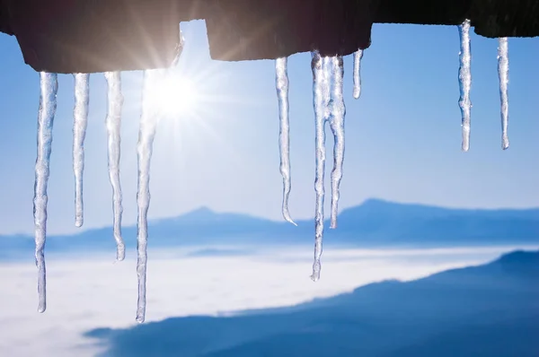 木造住宅の屋根の上のつららと冬の背景 山の村で解凍します 青い空と天気 — ストック写真