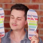 Man showing rainbow flip flops on brick wall background