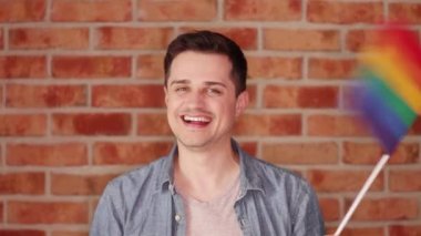 Gökkuşağı bayrağı tuğla duvar arka plan üzerinde oynamaktan mutlu adam