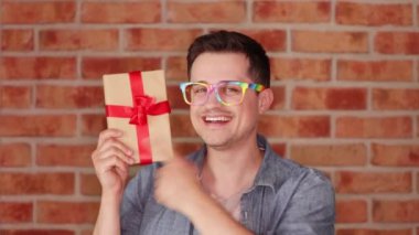 Mutlu adam tuğla duvar arka plan üzerinde kırmızı yay ile mevcut tutan gözlük