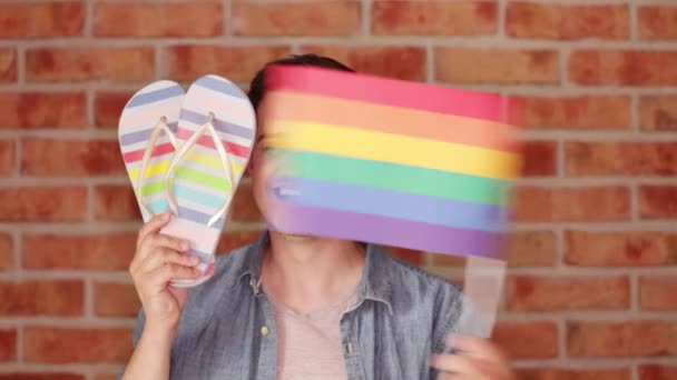 Happy Man Holding Flip Flops Playing Rainbow Flag Brick Wall — Stock Video