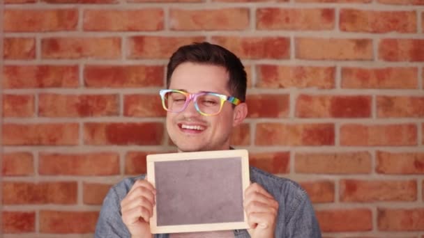 Hombre Feliz Anteojos Sosteniendo Diminuta Pizarra Sobre Fondo Pared Ladrillo — Vídeos de Stock