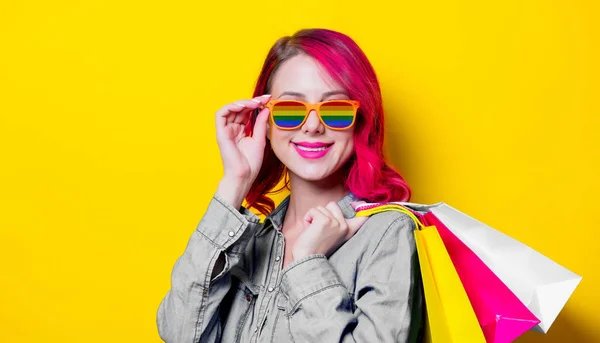 Menina em óculos de sol arco-íris segurando um sacos — Fotografia de Stock