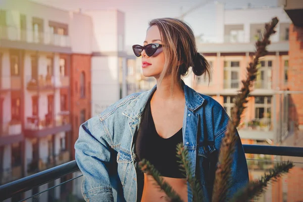 Девушка в джинсах и солнцезащитных очках на балконе — стоковое фото