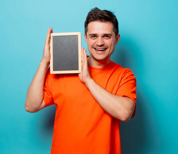 Ο άνθρωπος σε πορτοκαλί μπλουζάκι με μικρό μαυροπίνακα — Φωτογραφία Αρχείου