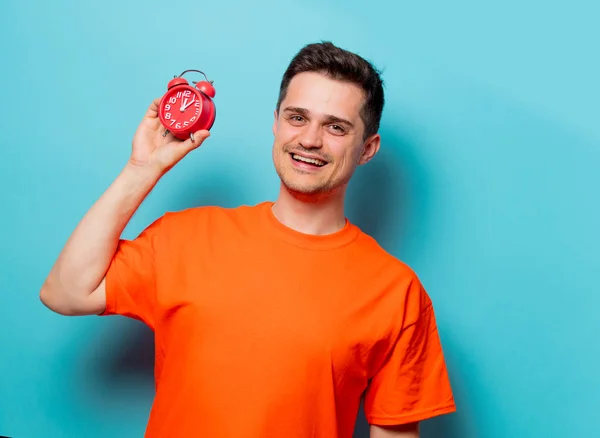 Homem em camiseta laranja com despertador vermelho — Fotografia de Stock