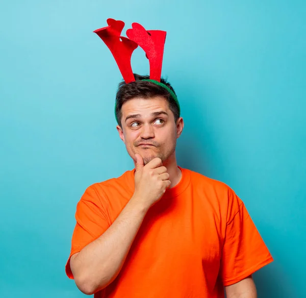 Mann in orangefarbenem T-Shirt mit weihnachtlichen Hirschhörnern — Stockfoto