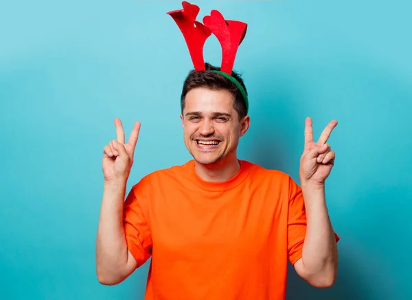 Homem em camiseta laranja com chifres de veado de Natal — Fotografia de Stock